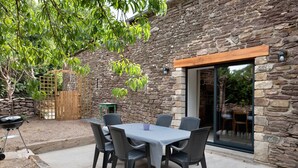 An outdoor patio with a stone wall, a wooden pergola, a table with chairs, and a grill. - La Maison de Gautro – Holiday Home with Terrace and Garden (Tréhorenteuc)