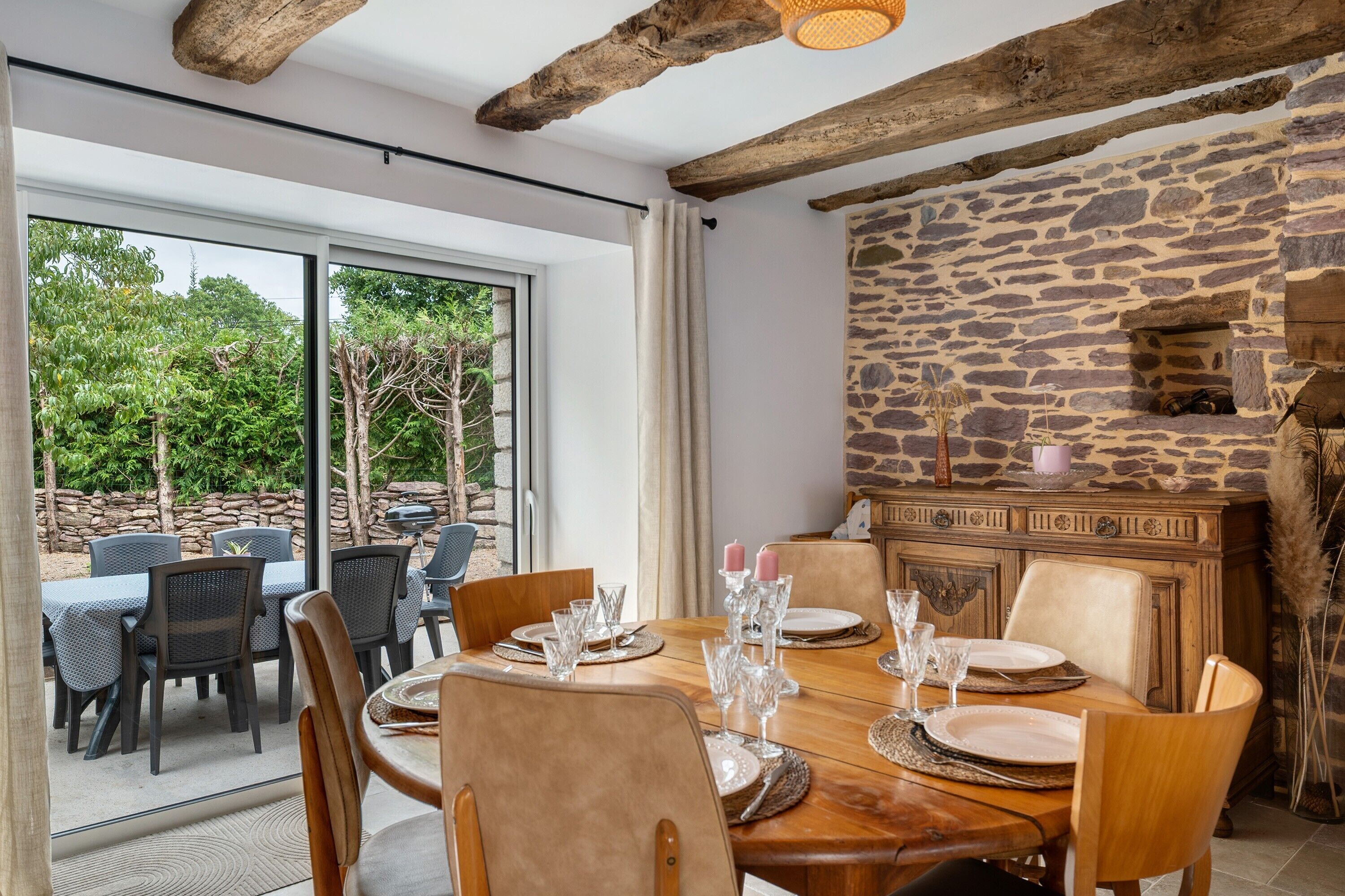 A dining area with a stone wall, wooden furniture, and a view of the outdoors.