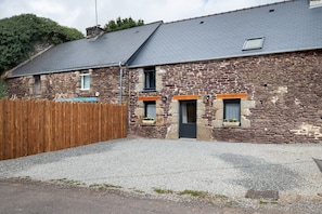 A stone building with a grey roof, wooden fence, and gravel driveway.
