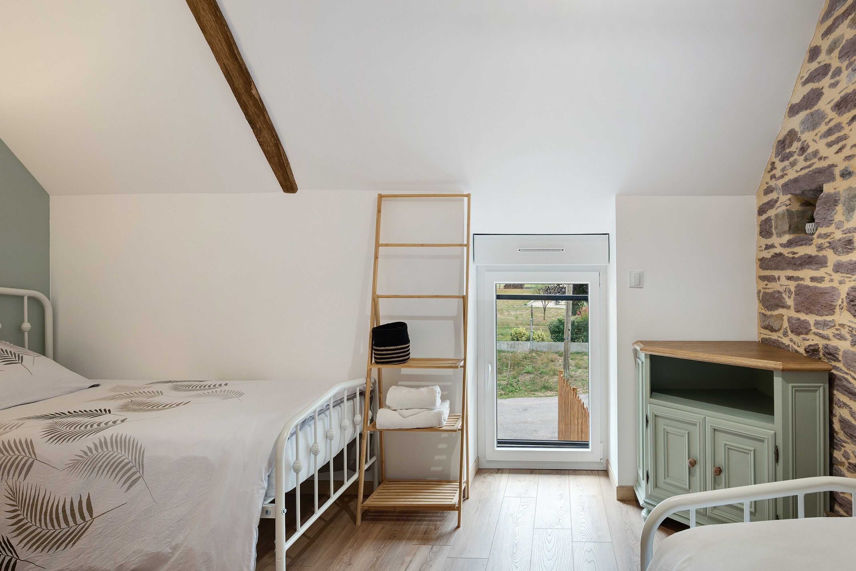 Une chambre avec un lit superposé, une échelle en bois, une petite étagère, une armoire verte et une vue sur l’extérieur par une porte vitrée.