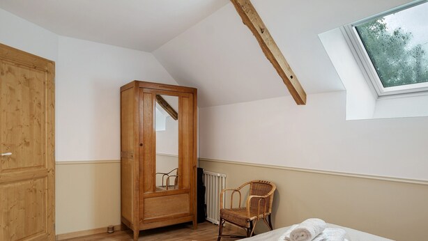 A bedroom with a wooden wardrobe, a wicker chair, and a bed with rolled towels. - La Maison de Gautro – Holiday Home with Terrace and Garden (Tréhorenteuc)