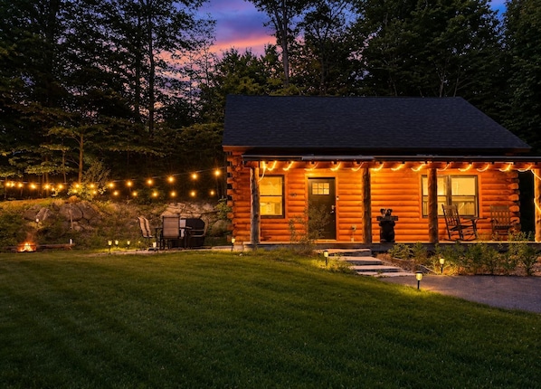 A log cabin with a porch, outdoor seating, and a stone fireplace.