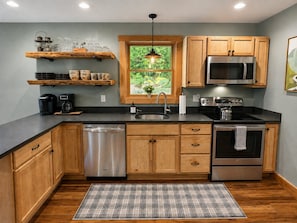 A modern kitchen with wooden cabinets, stainless steel appliances, and a window with a view of greenery.