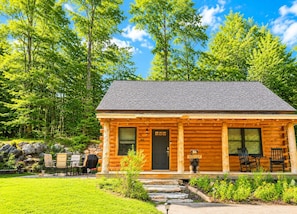 A log cabin with a porch, a welcome sign, and outdoor seating.