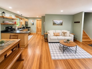 A modern kitchen with wooden cabinets, a dining area with a bench, and a living room with a sofa and coffee table.