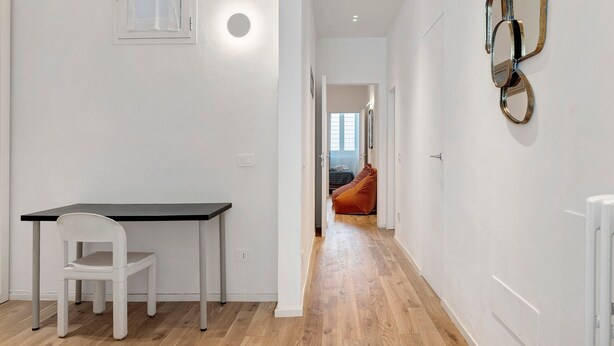 A hallway with a white wall, a door, a radiator, and a bed in the background. - Spazio Beccaria with Private Garden - Florence (Florence)