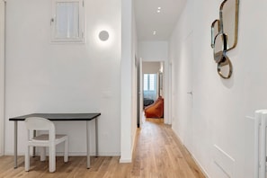 Ein Flur mit weißer Wand, einer Tür, einem Heizkörper und einem Bett im Hintergrund.