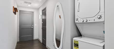 A laundry room with a front-loading washer and dryer, a towel rack, and a door leading to another room.