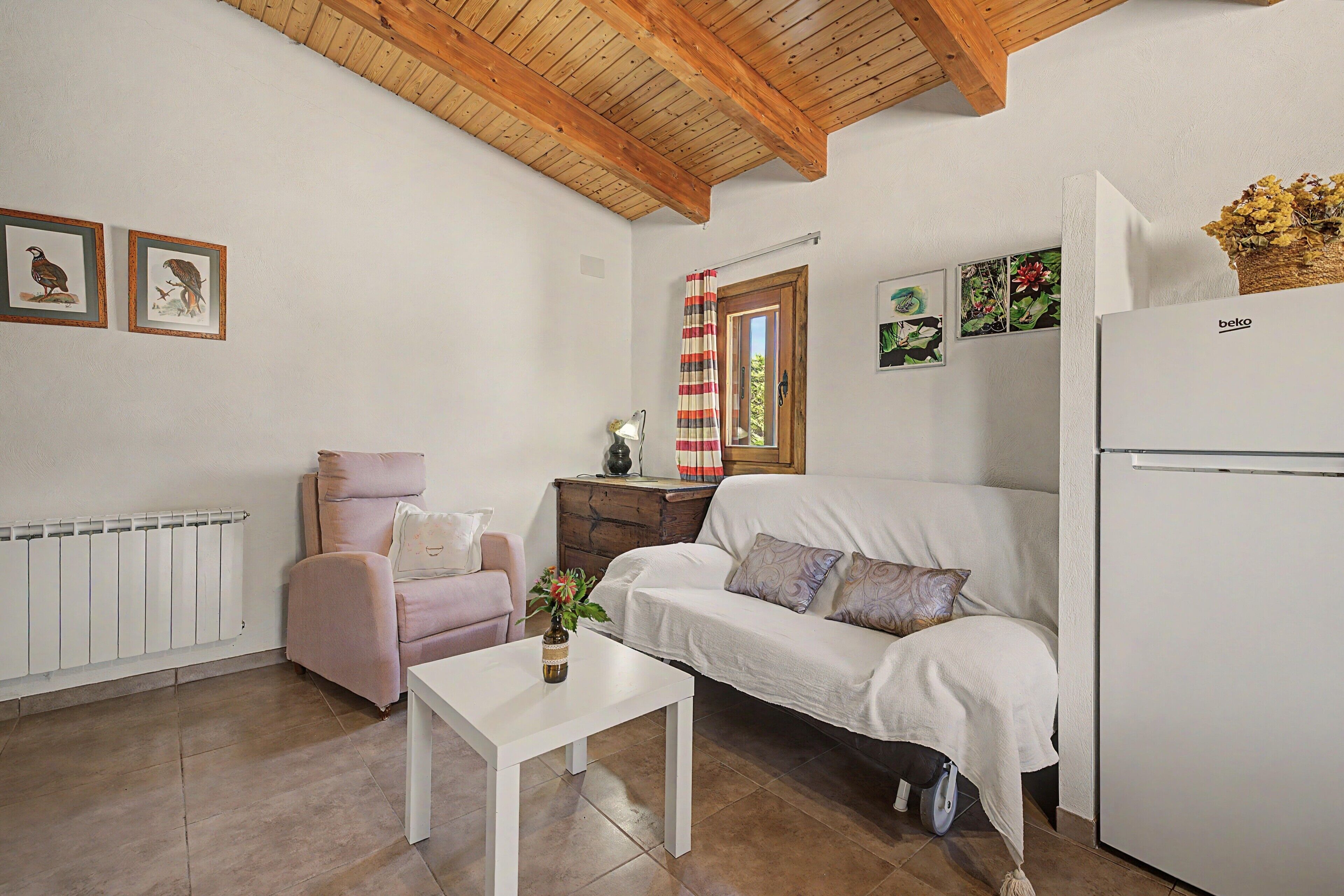A cozy room with a white sofa, a pink armchair, a small table, and a white refrigerator.