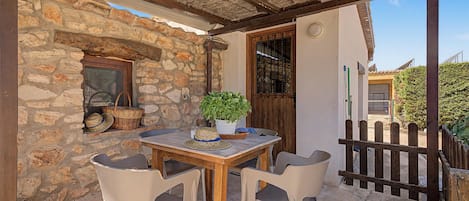 A stone wall with a window and a door, a table with chairs, and a potted plant.