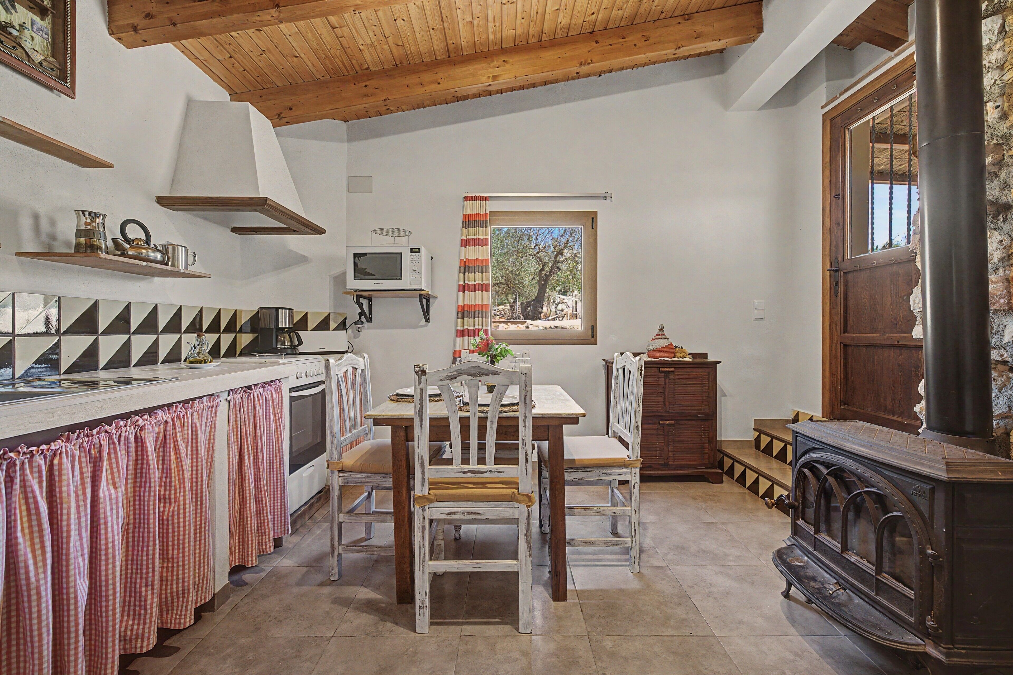 Une cuisine avec un plafond en bois, une table à manger avec des chaises, un four à micro-ondes et une fenêtre avec des rideaux.