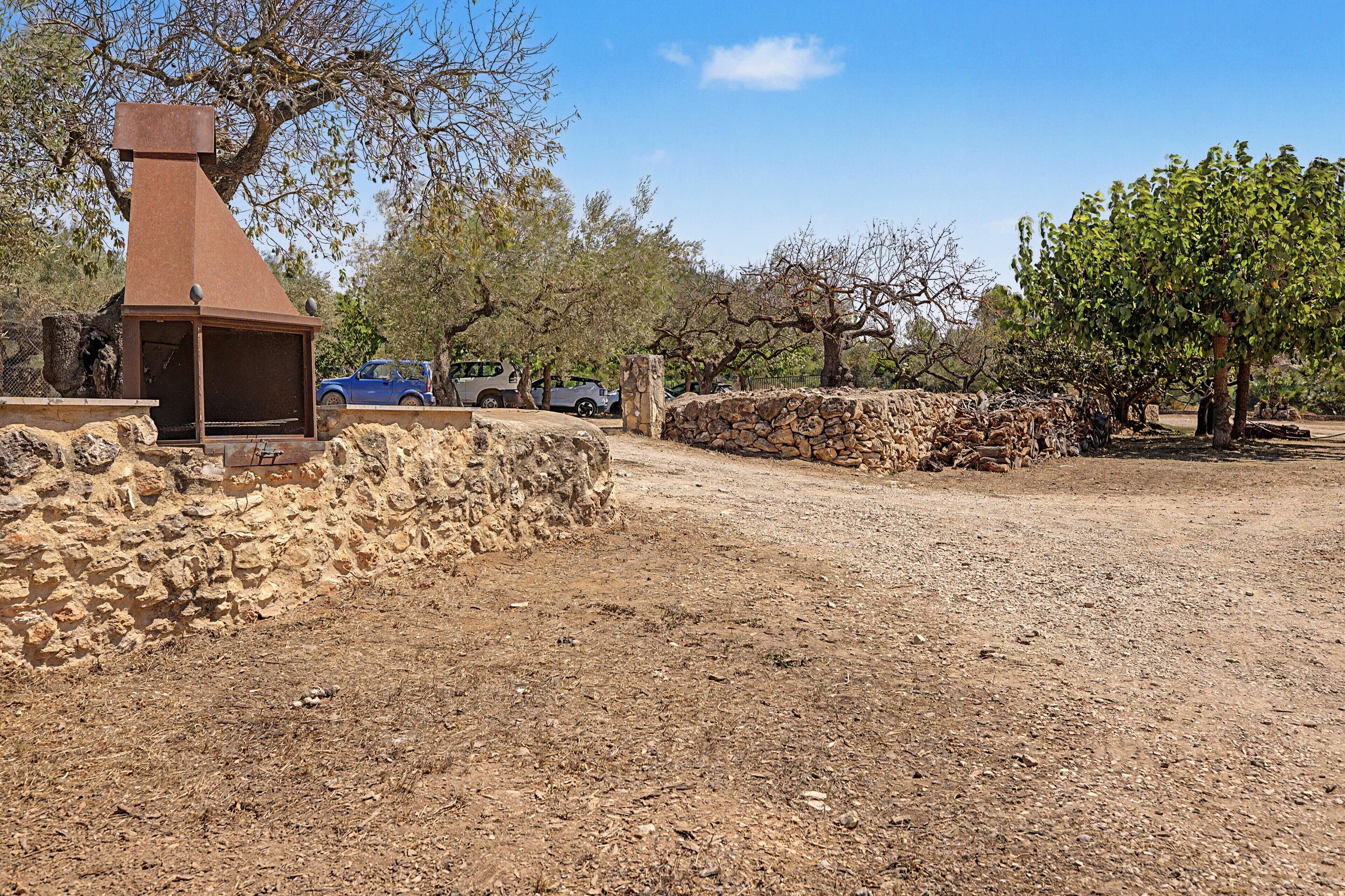 A rustic outdoor area with a stone wall, a metal structure, and parked cars.