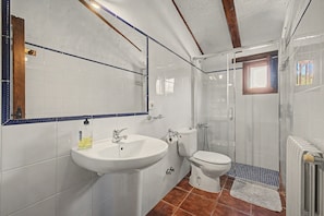 Une salle de bain avec un lavabo, des toilettes et une douche, le tout de couleur blanche.