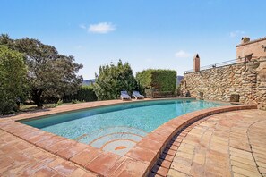 Une piscine avec un mur en pierre et un fauteuil de relaxation.