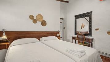 A hotel room with two beds, a desk, a chair, a mirror, and decorative wall art.