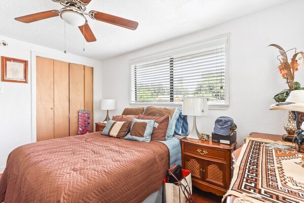 A bedroom with a bed, a ceiling fan, a window with blinds, a nightstand, and a lamp. - Buck Street - Houston (Houston)