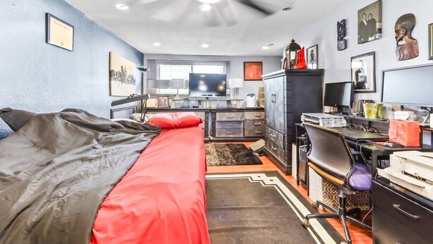 A bedroom with a bed, a desk, a chair, a computer, and a ceiling fan. - Buck Street - Houston (Houston)