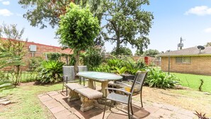 An outdoor patio with a stone table and metal chairs, surrounded by greenery and a brick wall. - Buck Street - Houston (Houston)