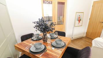 A dining area with a wooden table set for four, surrounded by chairs, and a vase with flowers on the table.