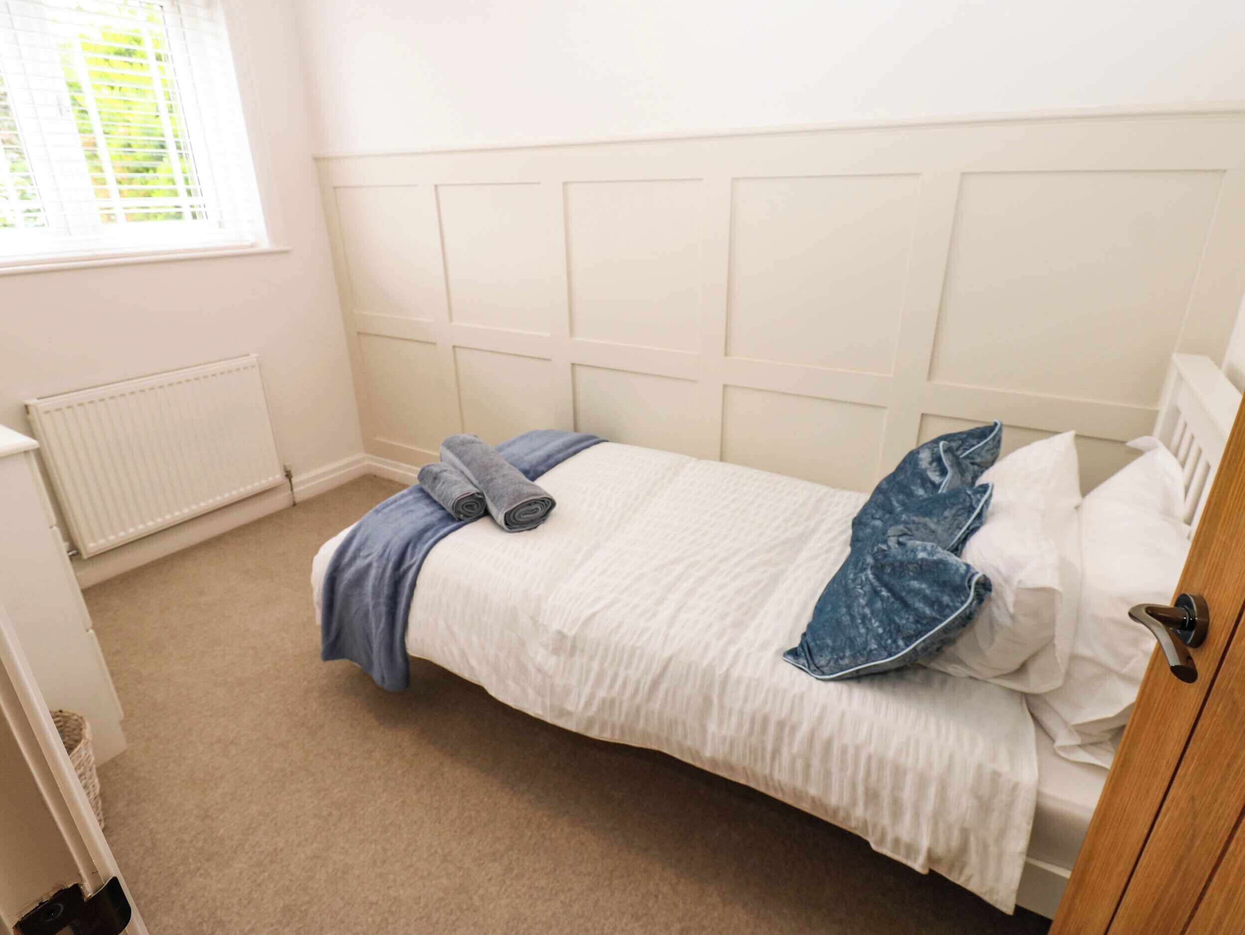 Ein Zimmer mit einem Einzelbett, einem weißen Kopfteil, einem Heizkörper, einem Fenster mit Jalousien und einem Holzschrank.
