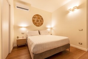 A bedroom with a bed, bedside lamps, a wall-mounted air conditioner, and a decorative wall piece. - Aura Suite & Private Spa (Palermo)