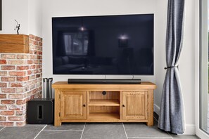 A flat-screen TV mounted on a wooden TV stand with a brick wall and a window with curtains.