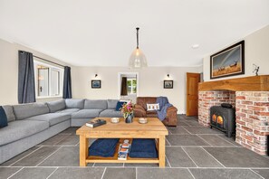 Ein Wohnzimmer mit einem Ecksofa, einem Holztisch, einem Kamin und einem großen Fenster.