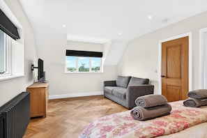 A bedroom with a bed, a grey sofa, a window with a view, a radiator, and a wooden door.