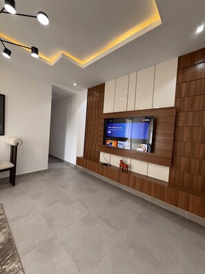 A modern living room with a flat-screen TV mounted on a wooden panel wall, recessed ceiling lighting, and a minimalist design. - Chic 1-Bedroom in Victoria Island with Pool, Fast Wi-Fi & 24/7 Power (Lagos)