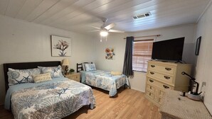 Ein Schlafzimmer mit zwei Betten, einem Schminktisch, einem Fernseher und einem Deckenventilator.