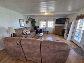 Ein gemütliches Wohnzimmer mit einer braunen Sofagarnitur, einem kleinen runden Couchtisch und einem an der Wand befestigten Fernseher.