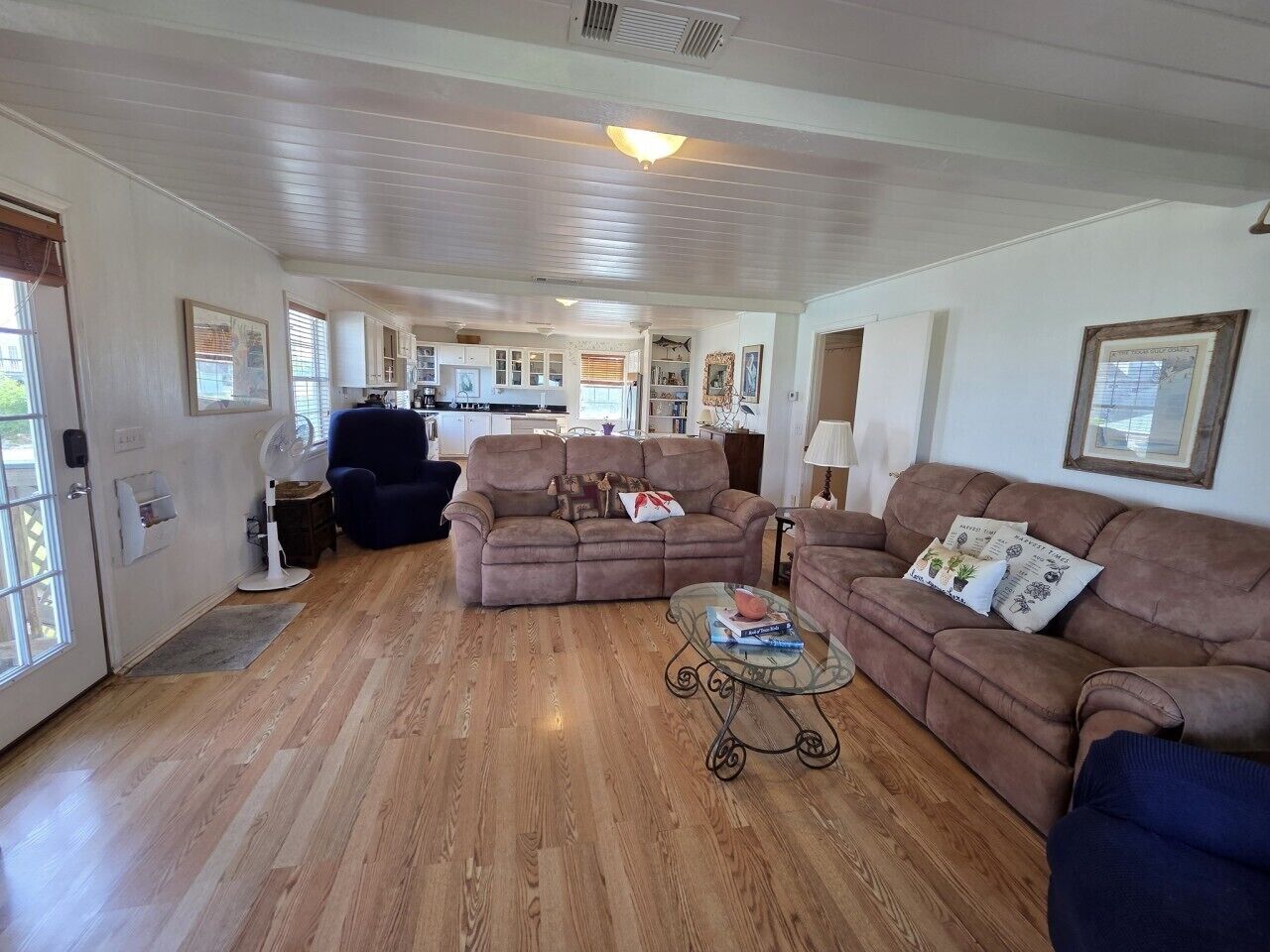 A spacious living area with a wooden floor, two sofas, a glass coffee table, and a kitchen in the background.