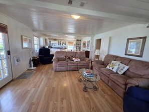 A spacious living area with a wooden floor, two sofas, a glass coffee table, and a kitchen in the background. - Great House with a View by the Short Jetty and Kingfisher Beach (Port O`Connor)
