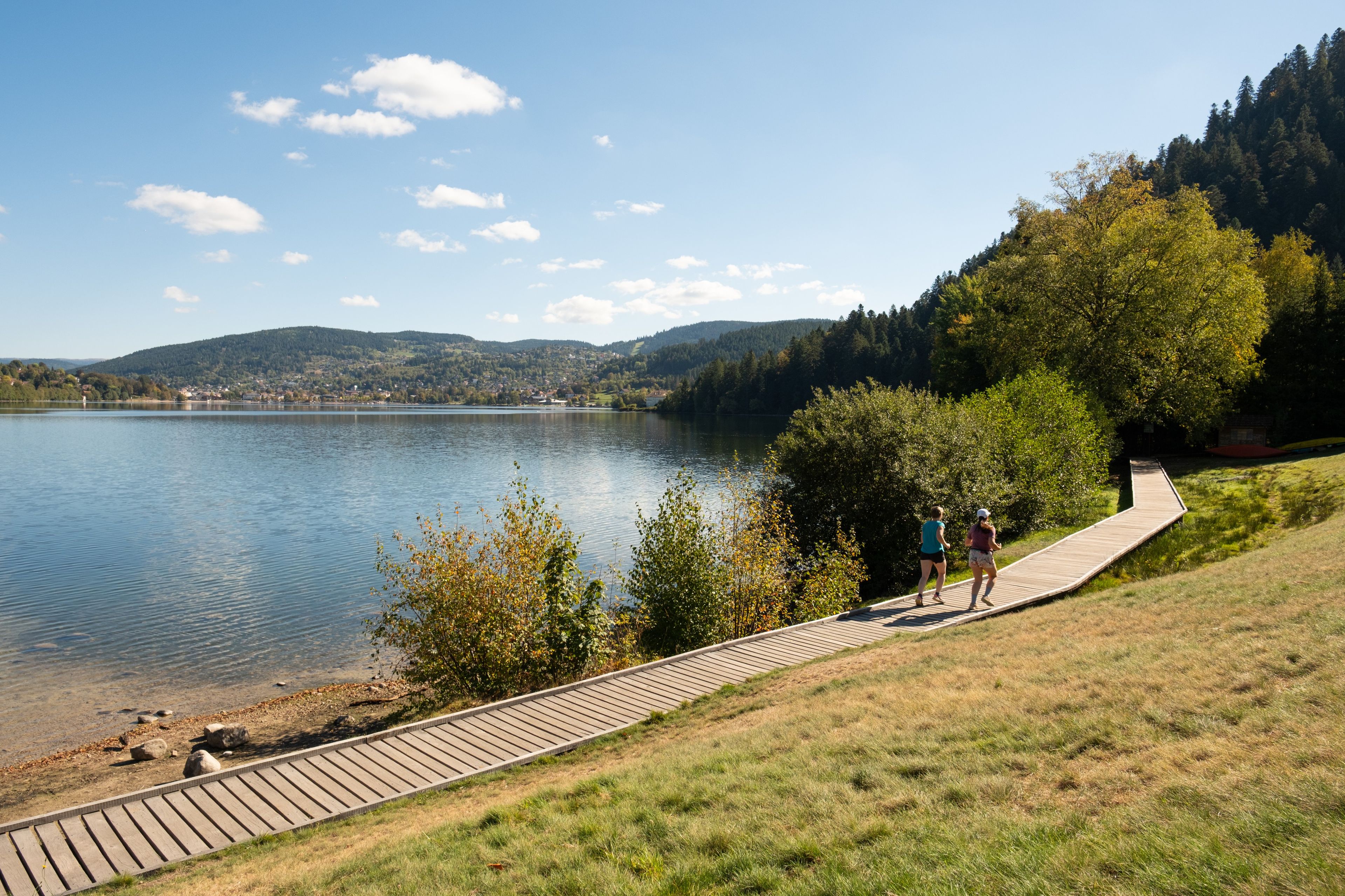 A wooden boardwalk leading to a lake with a clear view of a distant town and hills.