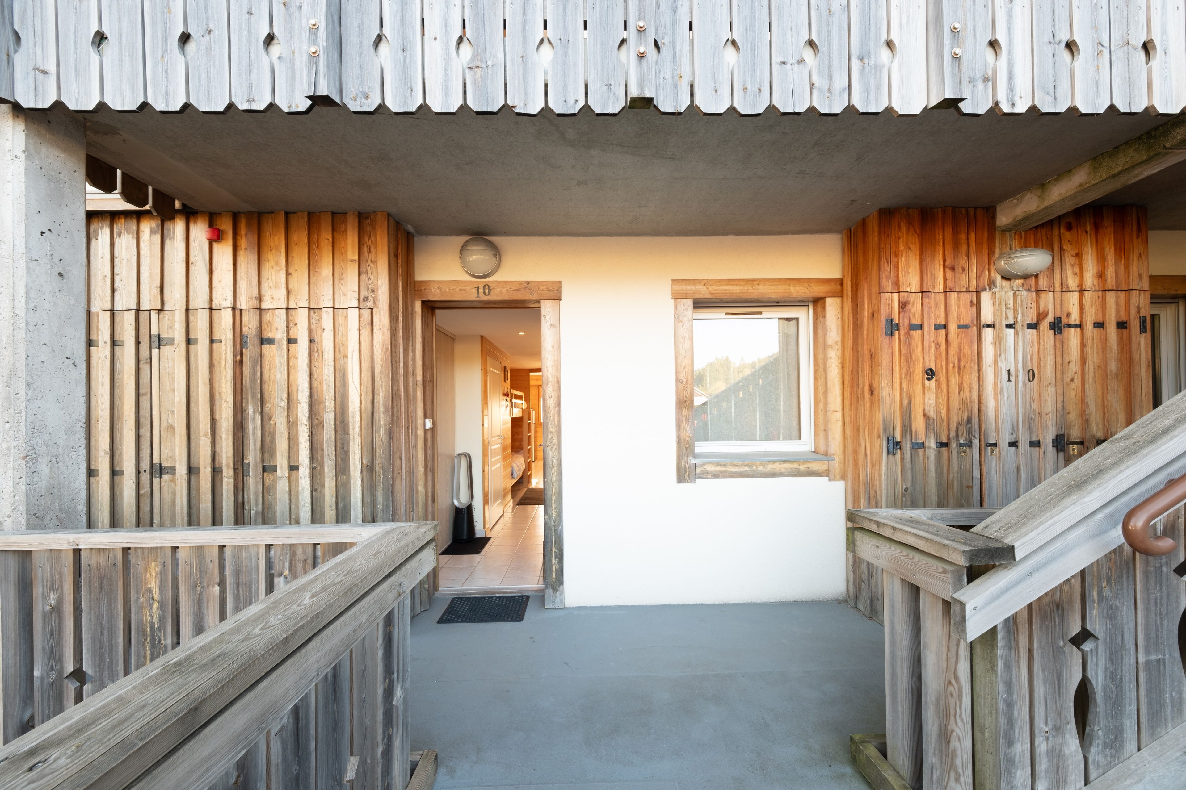 Una escalera de madera que lleva a una habitación con una ventana, una puerta con un número y un pasillo con una puerta.