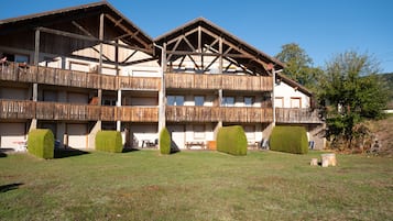 Un edificio de varios pisos con balcones, techo plano y un patio con césped.