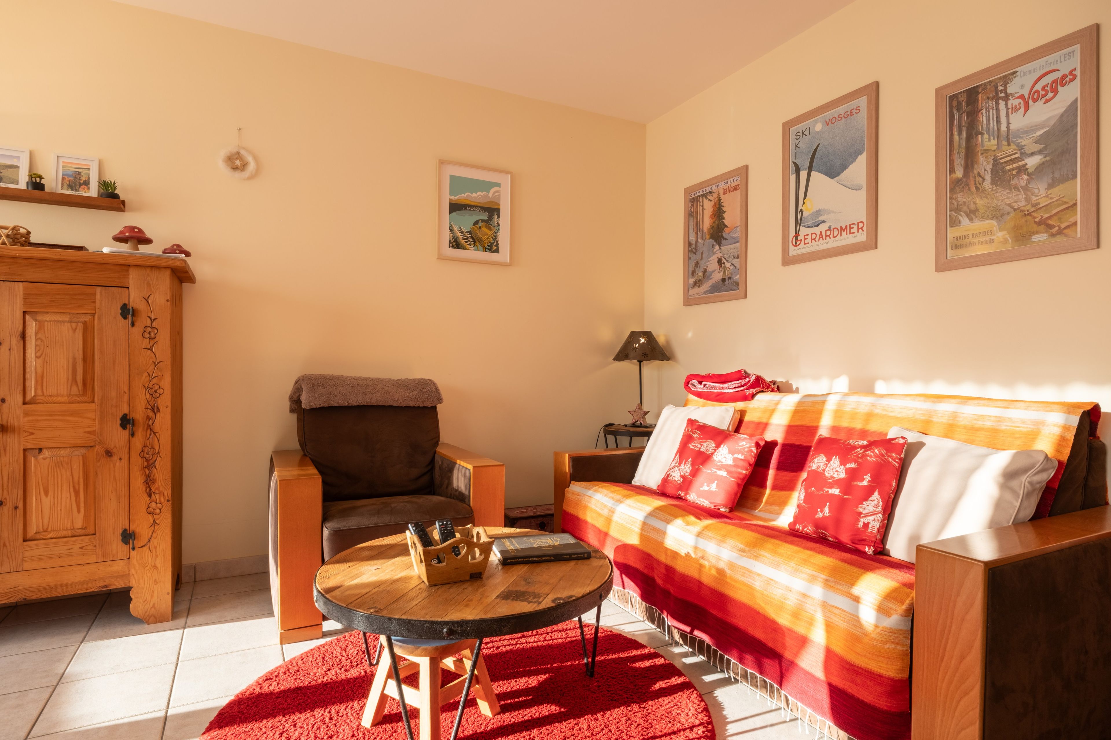 Un salon chaleureux avec un meuble en bois, un fauteuil en cuir marron, un canapé agrémenté de coussins rouges et blancs, et un tapis rouge.