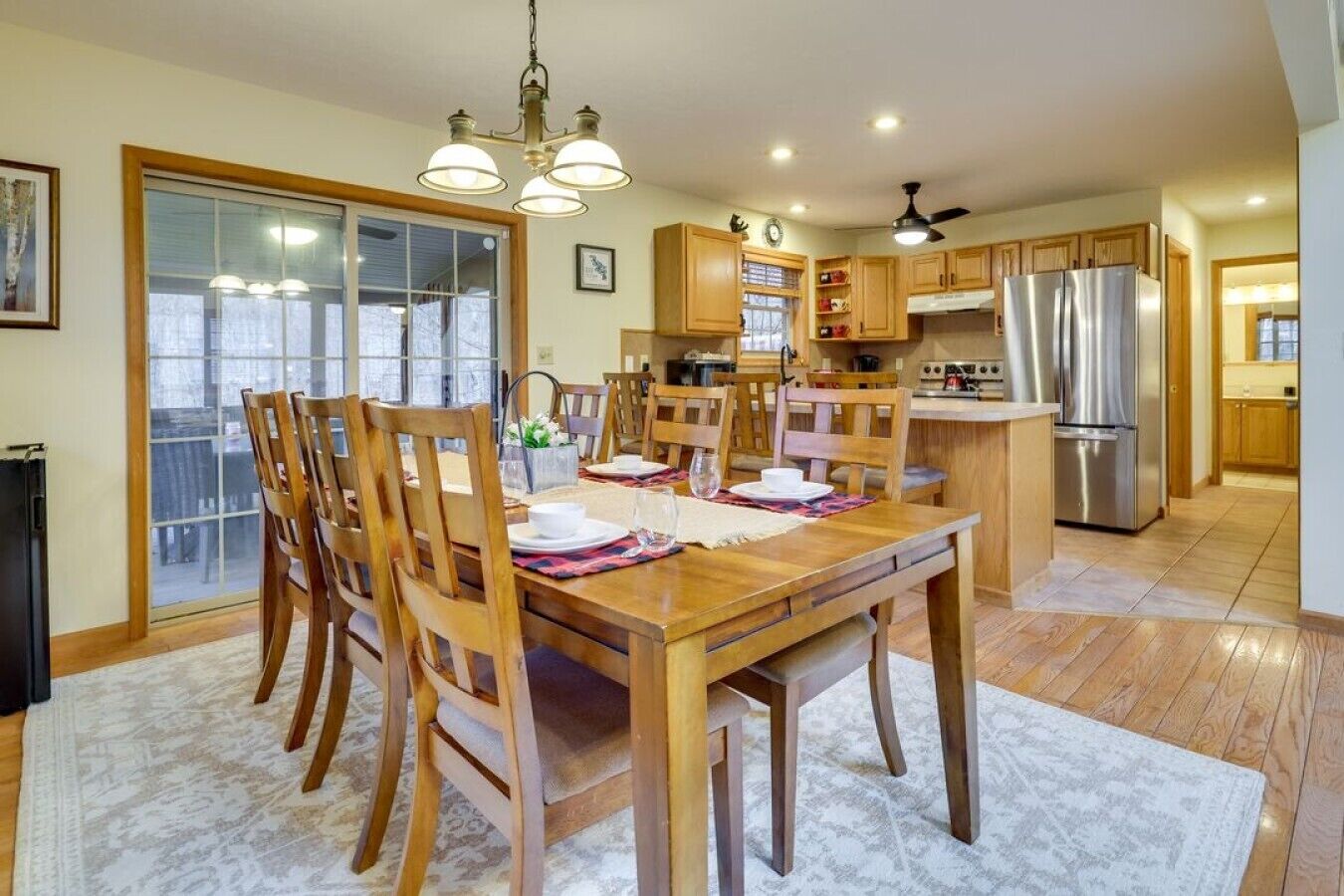 Un amplio comedor con mesa y sillas de madera, una cocina con armarios de madera y electrodomésticos de acero inoxidable, y un ventanal corredero que da a un balcón.