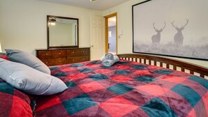 Een slaapkamer met een bed, een plafondventilator, een kaptafel, een spiegel en een groot, ingelijst beeld van herten aan de muur.