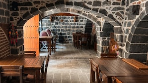 A stone-walled dining area with wooden tables and benches, a stone fireplace, and a rustic ceiling. - Taş Avlu Konaklama (Diyarbakir)