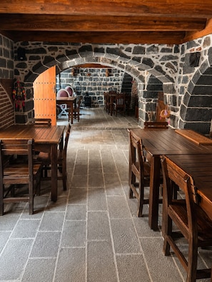 A stone-walled dining area with wooden tables and benches, a stone fireplace, and a rustic ceiling. - Taş Avlu Konaklama (Diyarbakir)