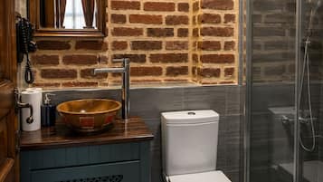 Une salle de bain avec un meuble-lavabo en bois, des toilettes blanches, une cabine de douche en verre et un mur en briques.