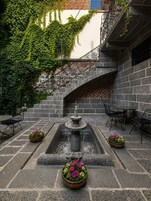 Un patio con una fuente de piedra, asientos exteriores y una escalera de ladrillo.