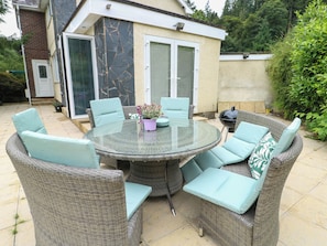 Eine Terrasse im Freien mit Korbmöbeln und einem Glastisch, umgeben von viel Grün.