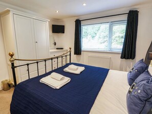 Ein Schlafzimmer mit einem Bett, einem Fernseher, einem Fenster mit Vorhängen und einer Heizung.