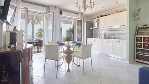 Una cocina moderna con armarios blancos, una mesa de comedor con sillas, un televisor y vistas al exterior.