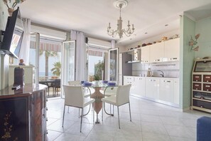 A modern kitchen with white cabinets, a dining table with chairs, a television, and a view of the outdoors. - Lo Scirocco (Andora)