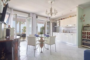 Una cocina moderna con armarios blancos, una mesa de comedor con sillas, un televisor y vistas al exterior.