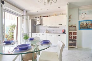 Una cocina moderna con armarios blancos, una mesa de comedor de vidrio y vistas al exterior.