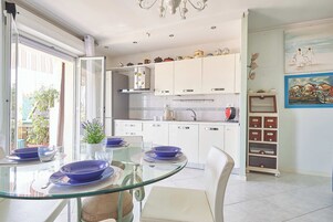 Una cocina moderna con armarios blancos, una mesa de comedor de vidrio y vistas al exterior.